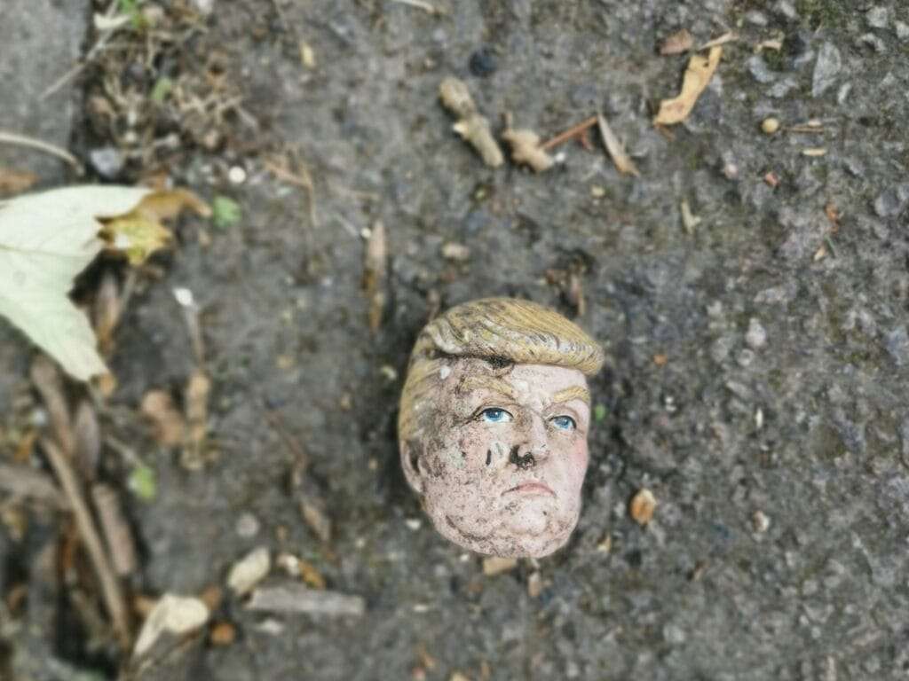 Aged head from a Trump doll laying on ground with other debris 